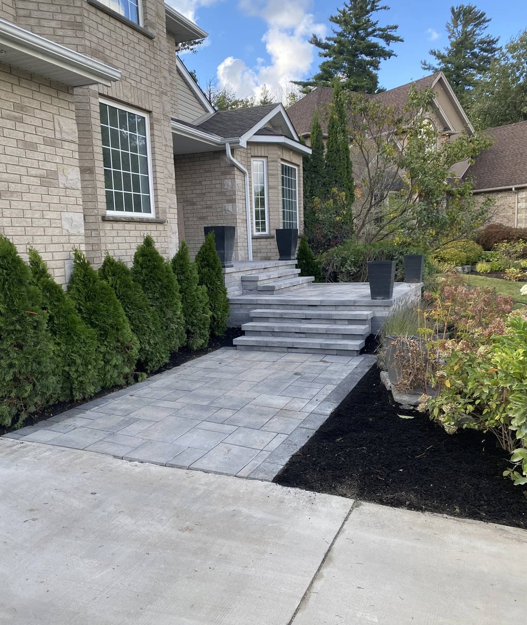 Paver walkway with stone steps leading to the front entrance of a large stone home
