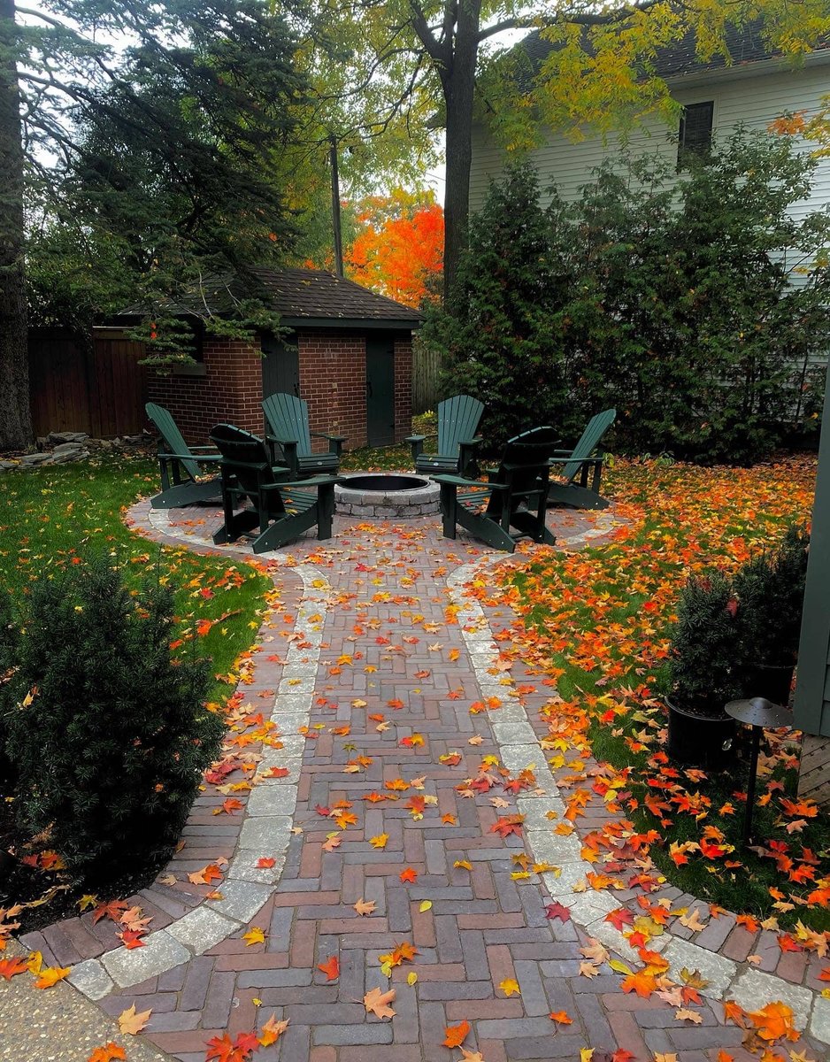 Brick paver walkway leading to a circular fire pit ringed by Adirondack chairs in autumn