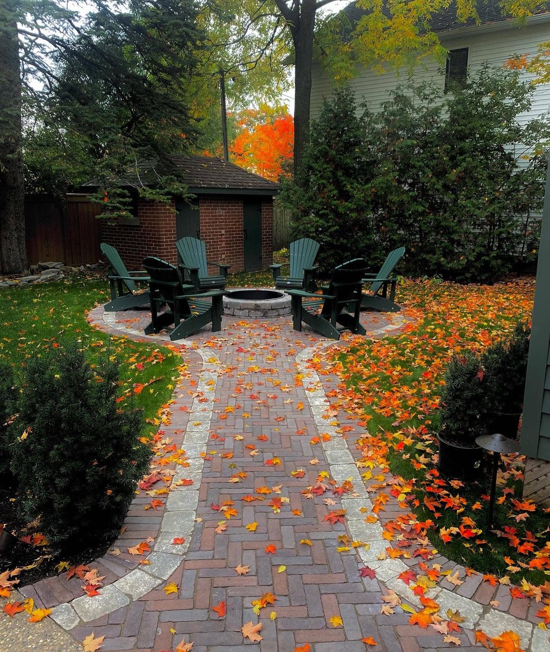 Brick paver walkway leading to a circular fire pit ringed by Adirondack chairs in autumn