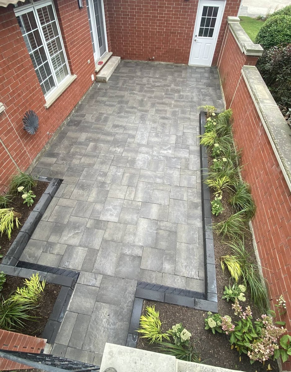Aerial view of a grey paver patio with planted border tucked between brick walls