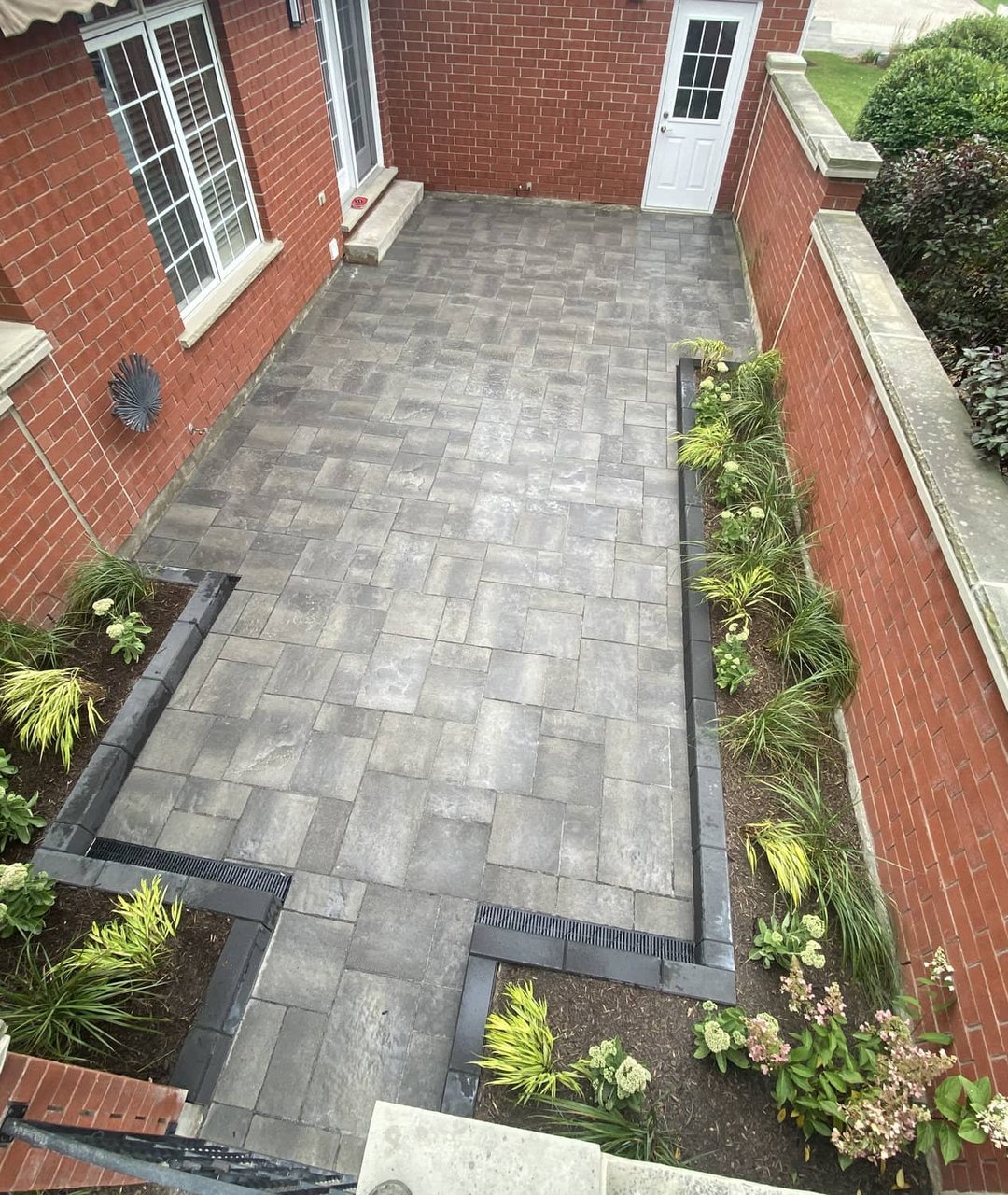 Aerial view of a grey paver patio with planted border tucked between brick walls