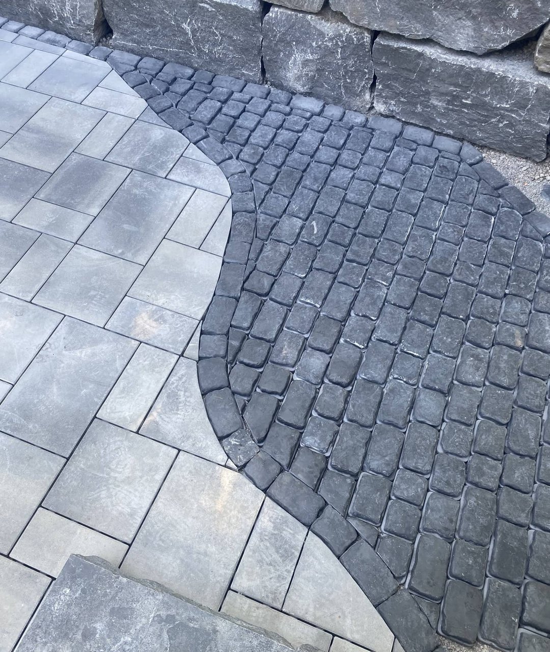 Detailed paver patio with curved cobblestone inlay against a stacked stone wall